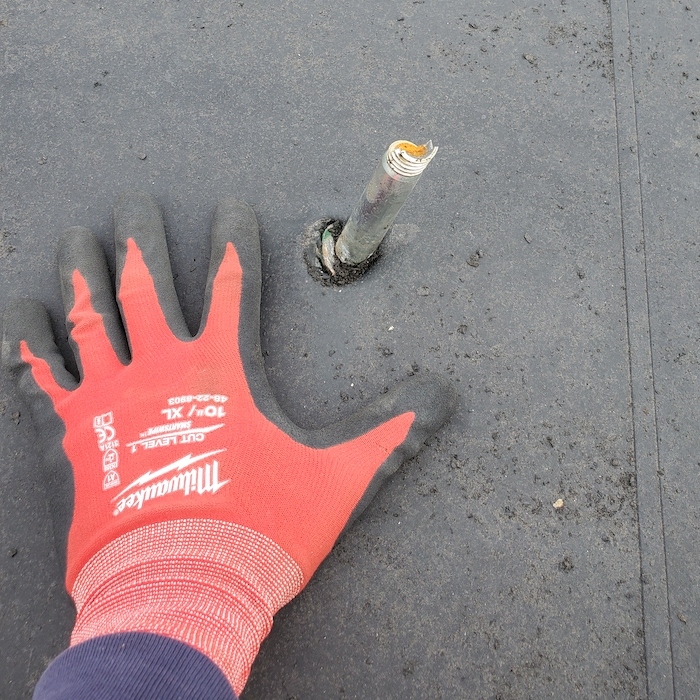 An orange workman's gloved hand next to an area of the roof that requires flashing.